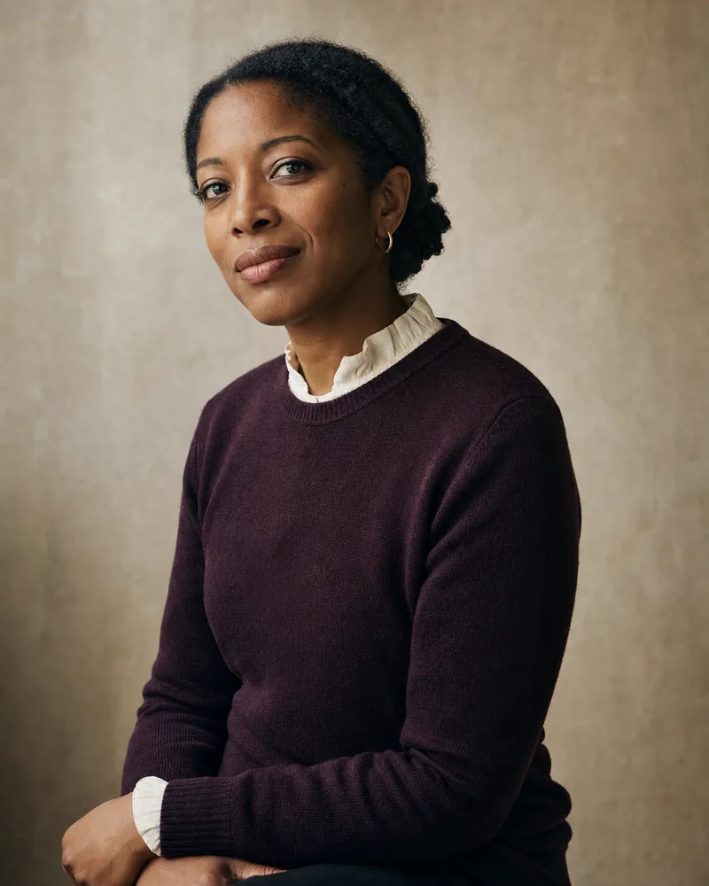 Editorial portrait of Dr Amara Bankole-Thomas, a Black British woman in her late thirties, framed against a soft pale-stone studio backdrop