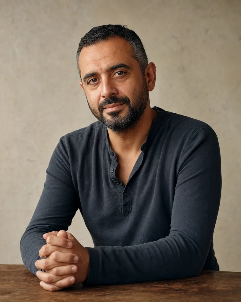 Editorial portrait of Yusuf Karaman, a British-Turkish man in his early forties with close-cropped dark hair, in a charcoal henley shirt